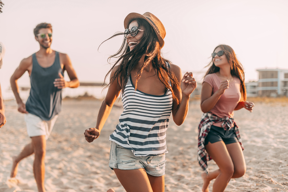 Group of young cheerful people running along the beach and looking happy.