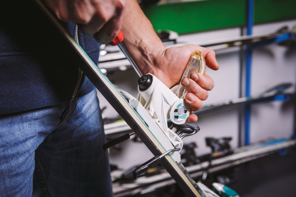 Close-up of a Caucasian man's hand using a hand-held screwdriver tool to tweak, twist bindings for ski boots in the workshop.