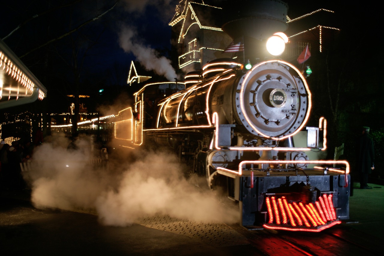 Christmas steam train spewing steam stopped with sparkling lights covering the train.