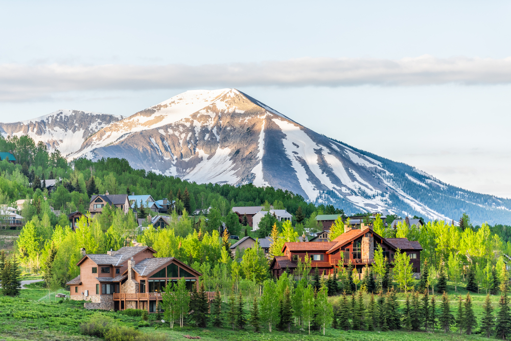 Mount Crested Butte, Colorado village in summer with colorful sunrise by wooden lodging houses on hills with green trees.