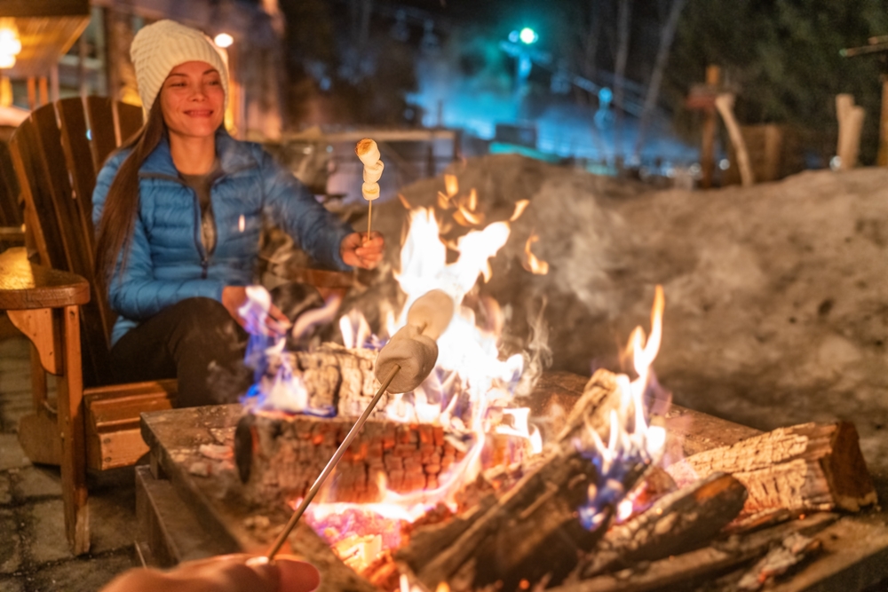 Winter campfire couple roasting marshmallows in fire pit for s'mores at ski resort.