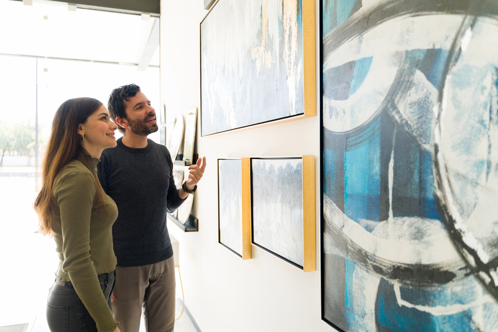 Good-looking young woman and man are talking about art while visiting a painting exhibition at an art gallery.