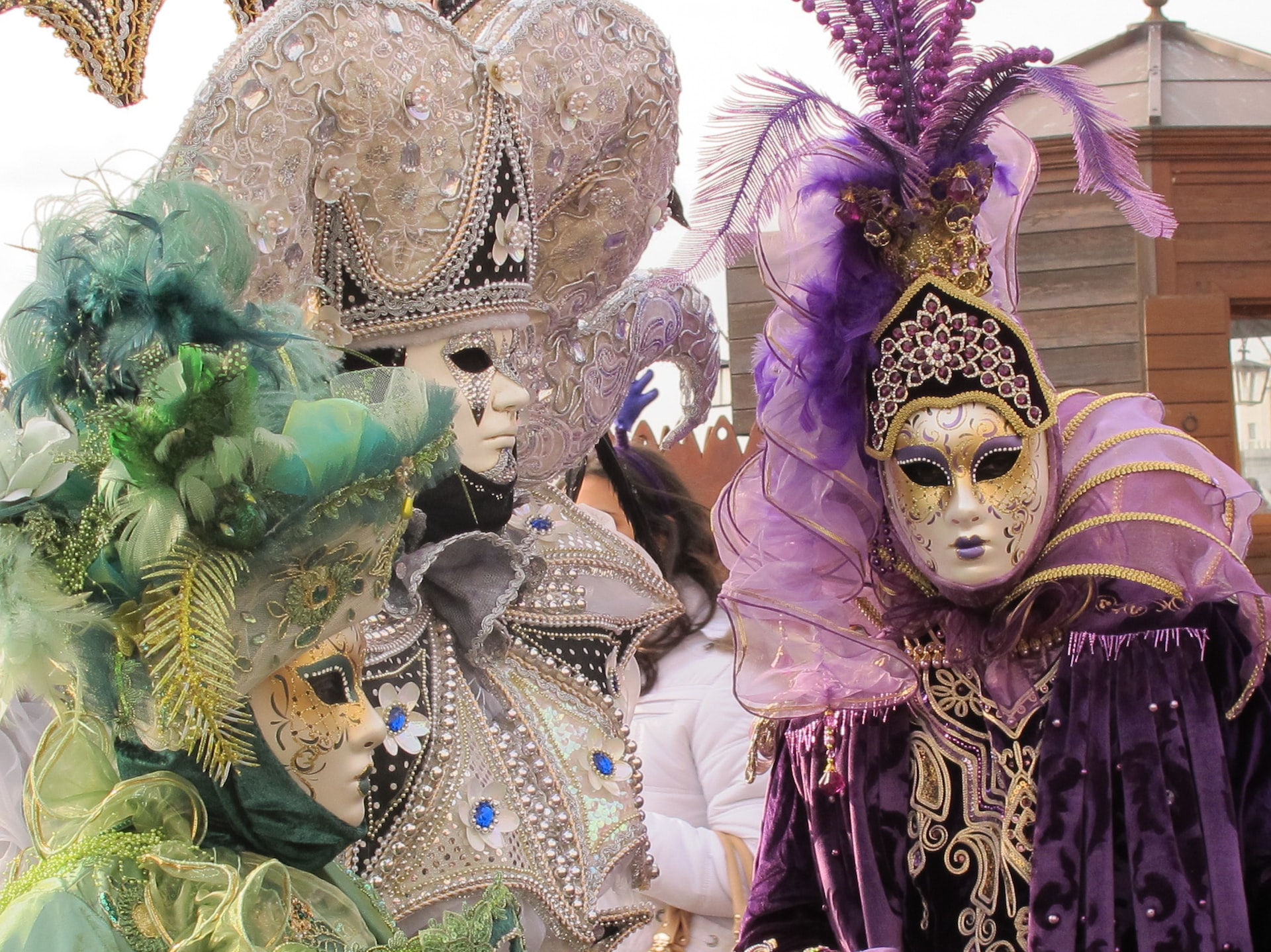 Three people in various colored outfits and masks for Mardi Gras.
