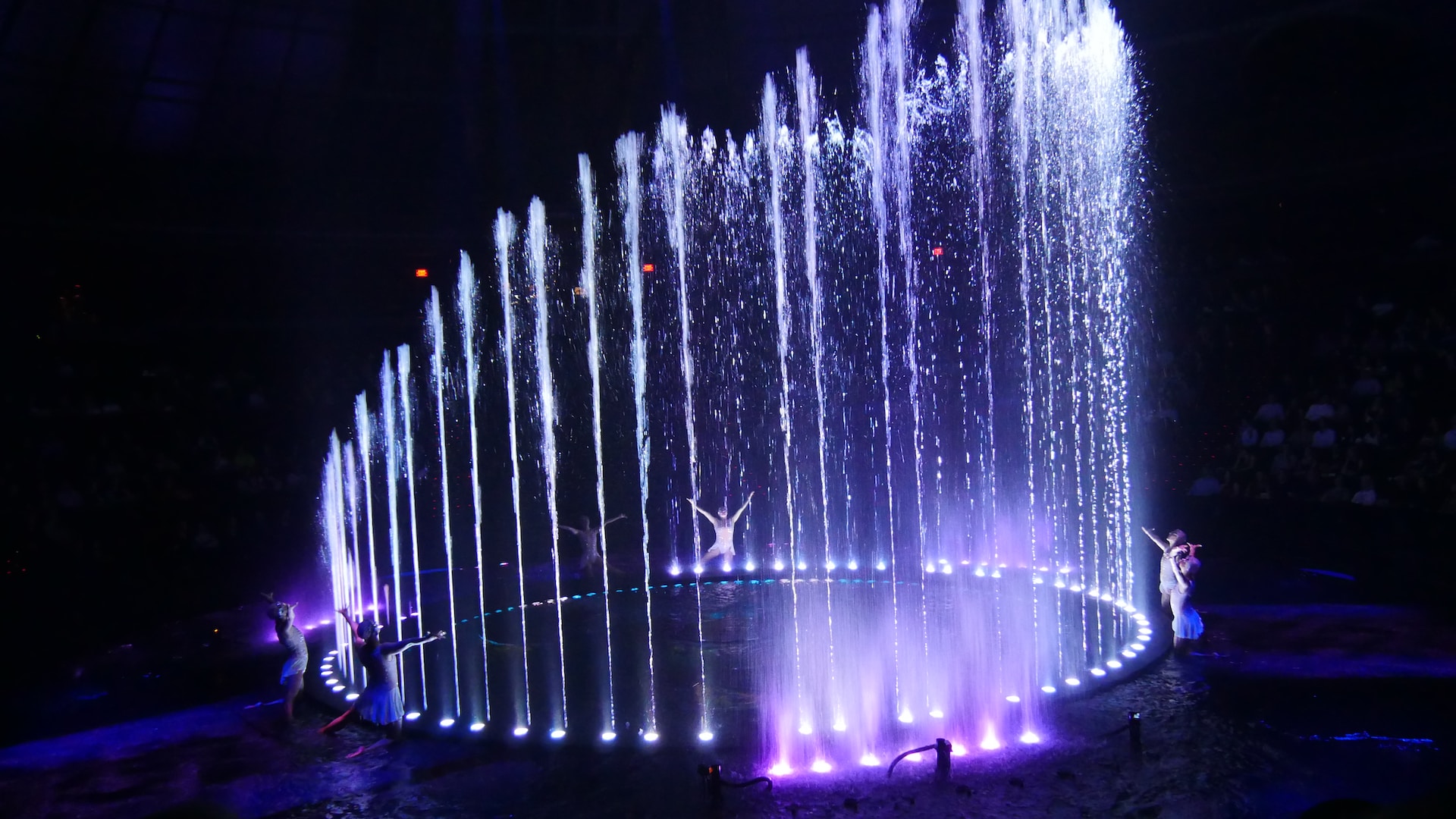 Dancers performing around a water and light show in the dark.