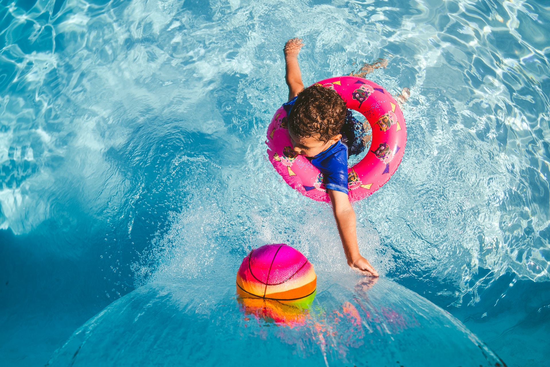 Boy in a floaty with a colorful ball in a pool beside a waterfall.