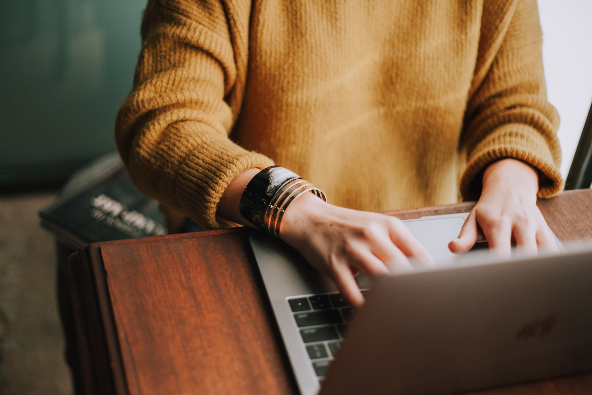 A woman in a comfy mustard-colored sweater typing on a laptop.