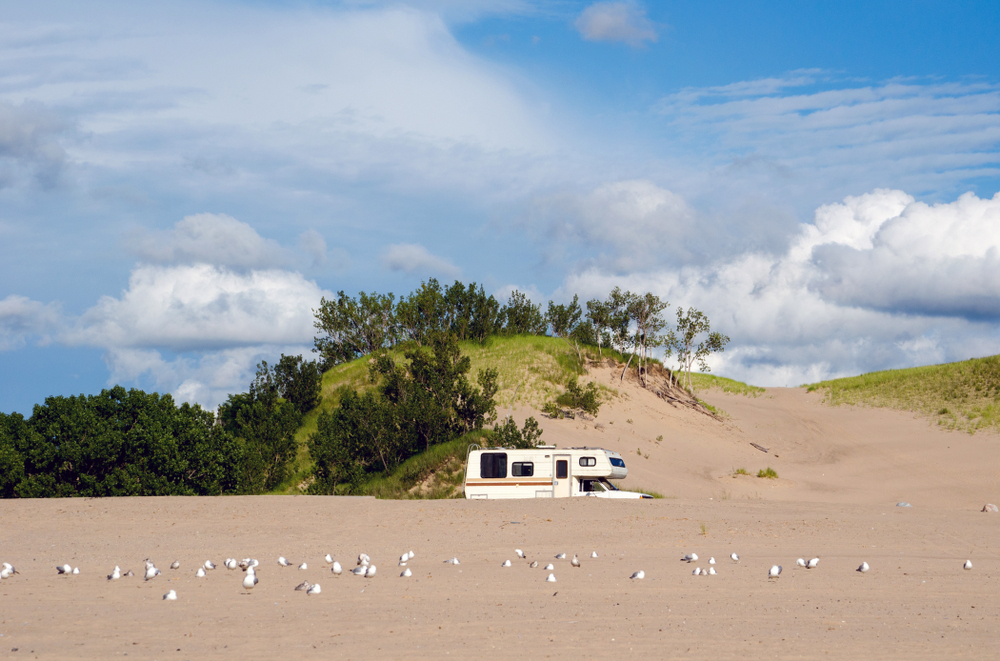 A motor home is parked near Lake Michigan and the dunes with seagulls.