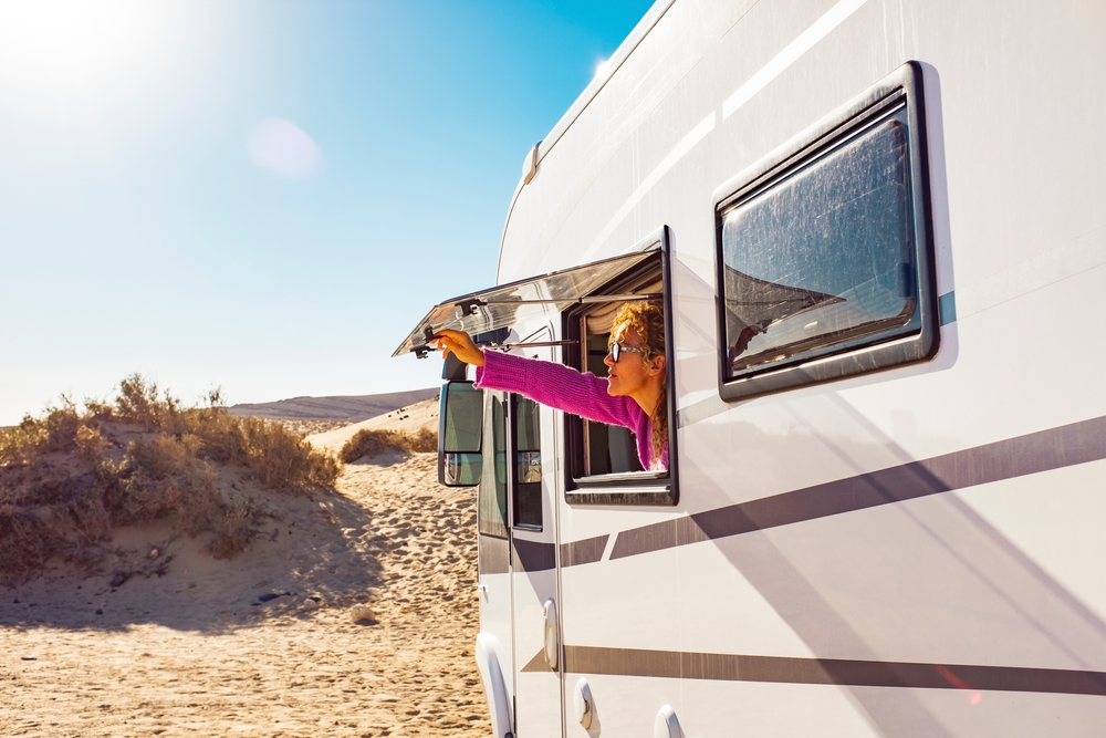 Woman opening an RV window at the beach during the day.