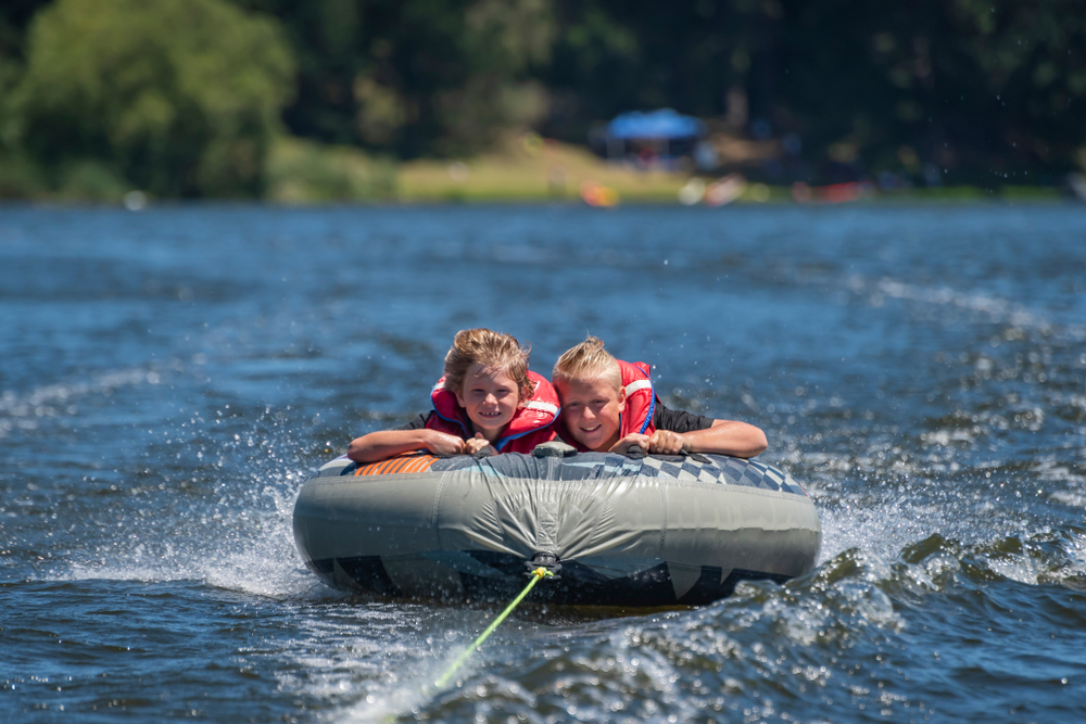 Children on an inflatable tube being towed behind a boat.