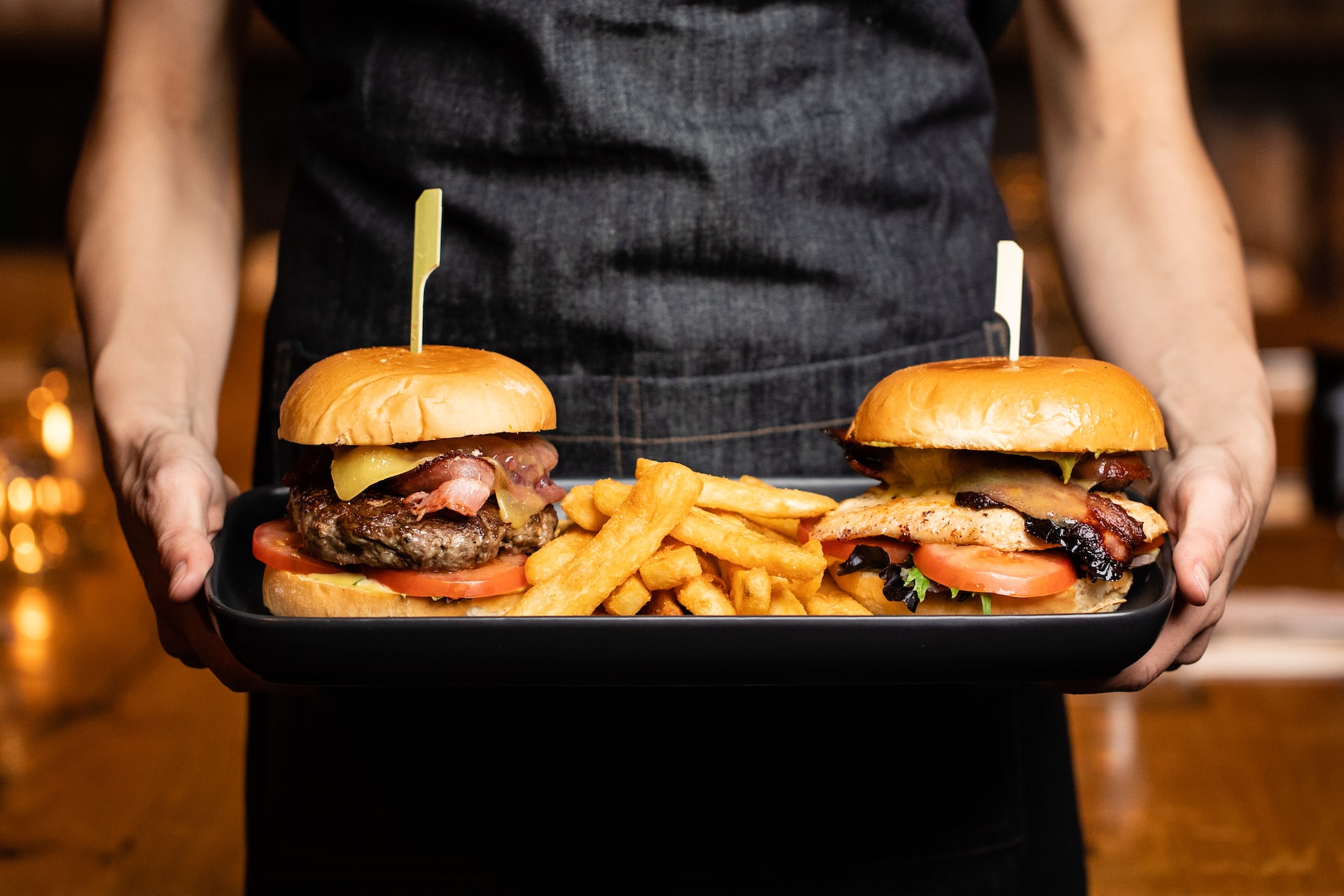 Two hamburgers being held on a tray by a server wearing a black outfit.