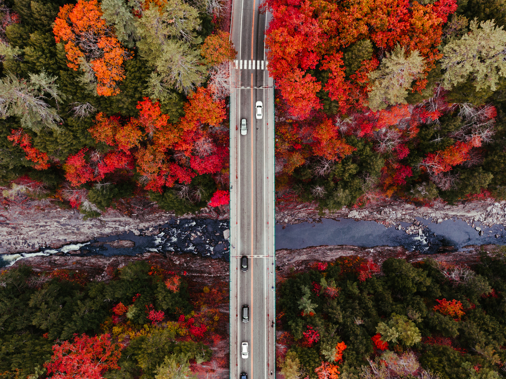 A drone shot of Quechee Gorge as seen from on high being divided by a bridge with cars moving across.