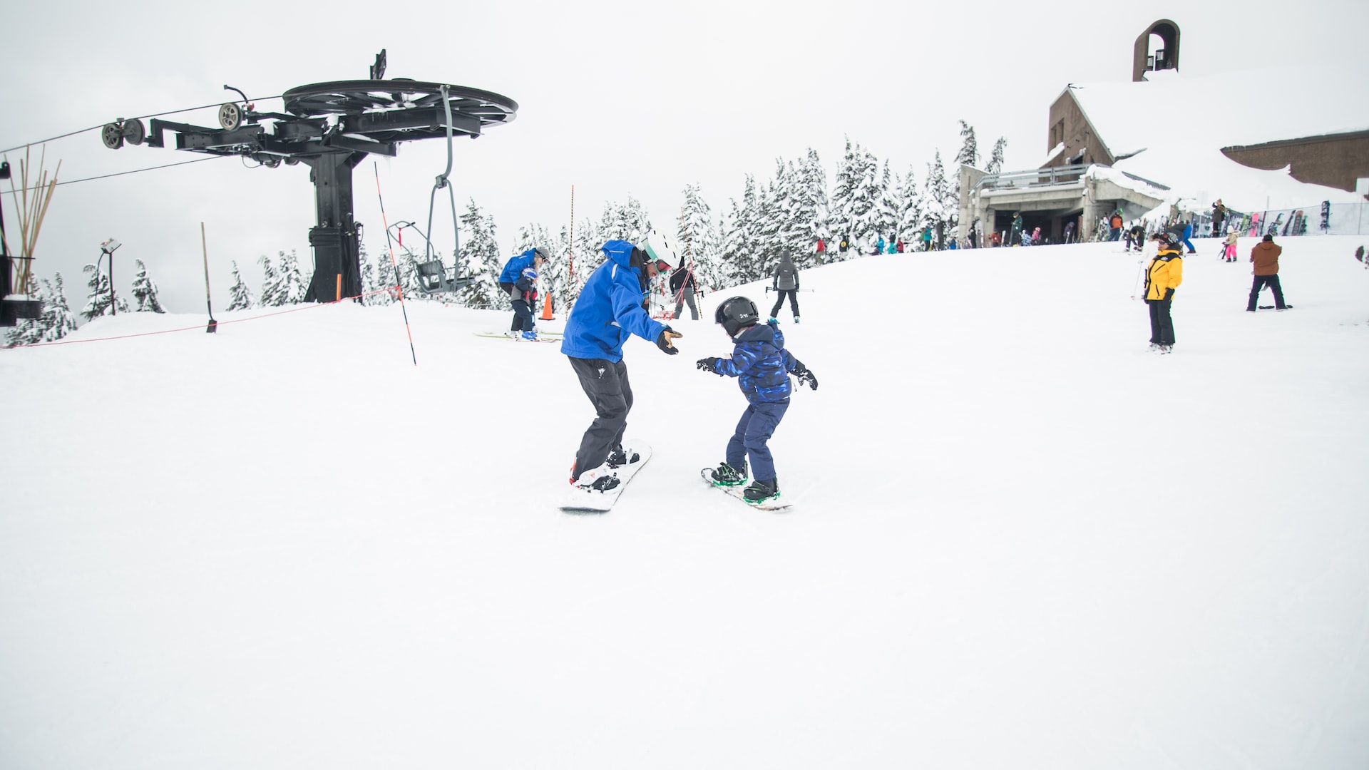 A child getting his first snowboarding lesson at the top of the mountain.