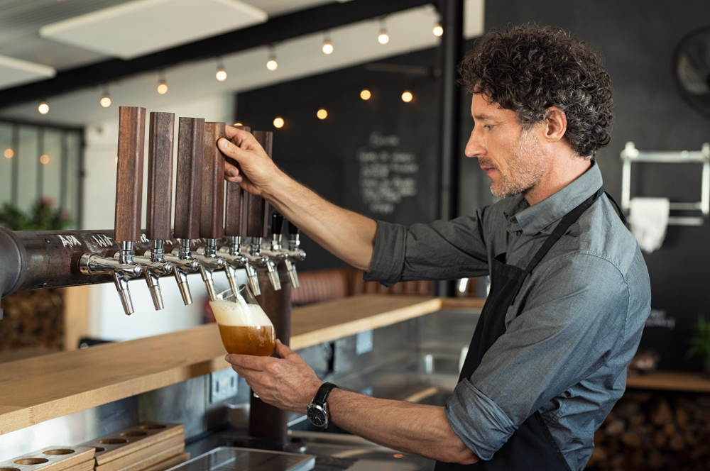 A bartender pouring beer on tap into a glass.