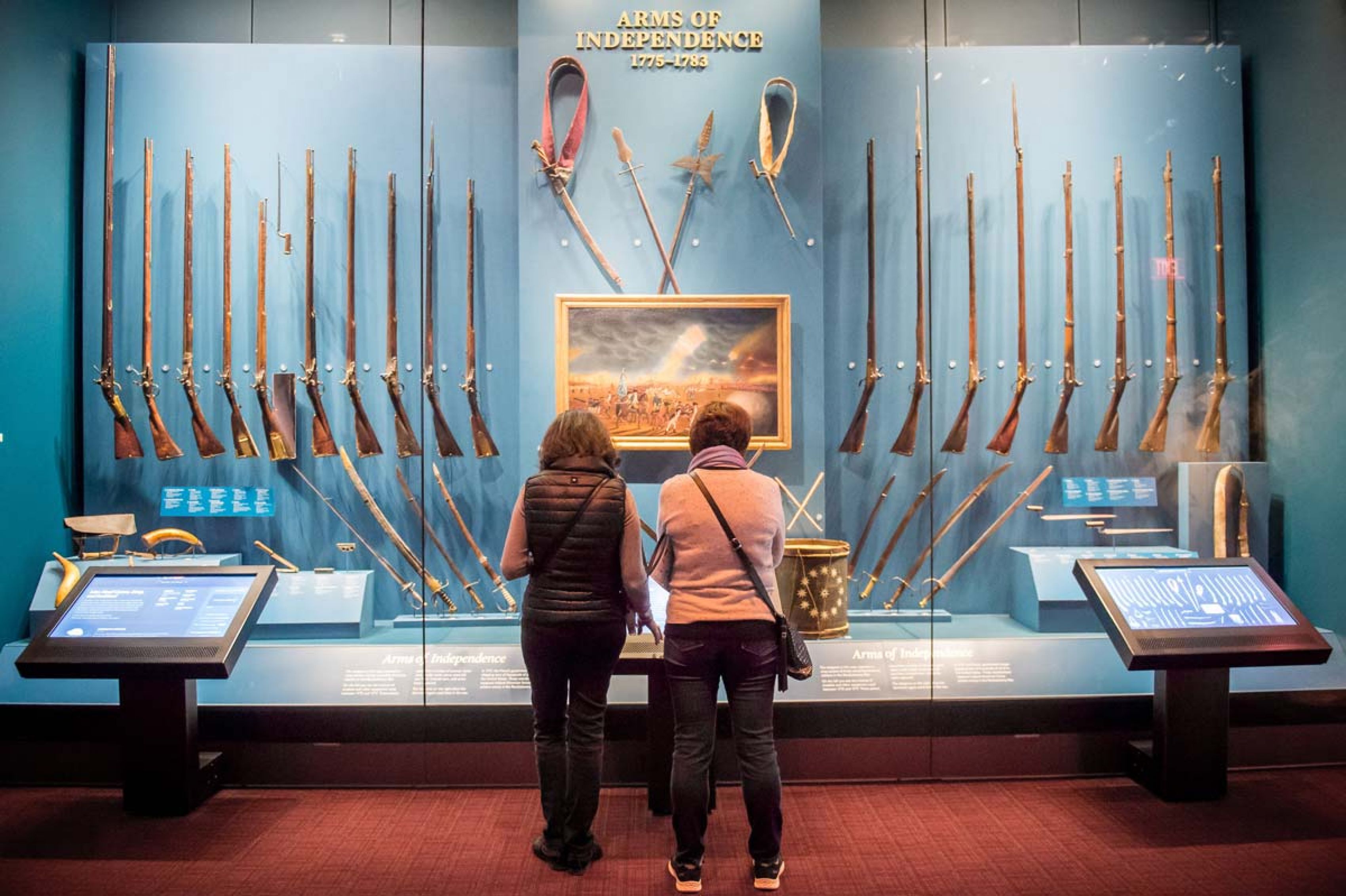 Two women with their backs turned viewing a display at the Museum of the American Revolution.