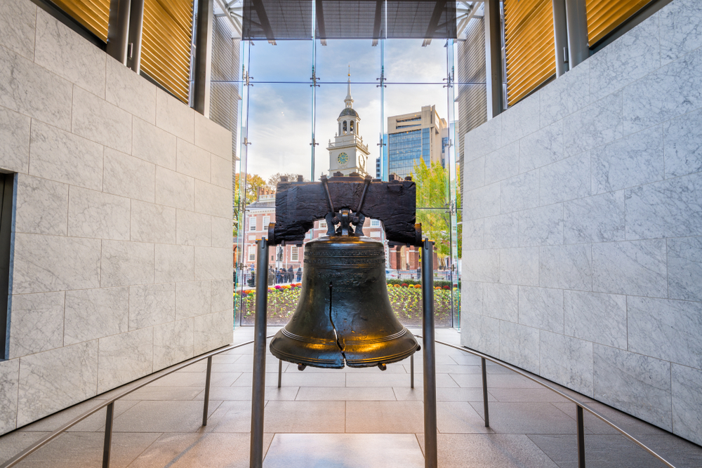 The Liberty Bell with Independence Hall seen through the tall see-through windows behind it.