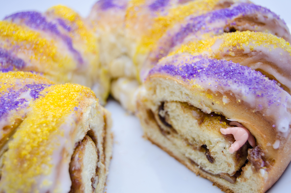 A multicolored King Cake with a plastic baby figurine sticking out.