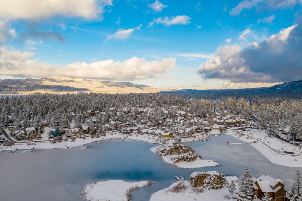 Aerial view of Big Bear Lake and town in California with the lake frozen on a sunny blue sky day in winter with pine trees below.