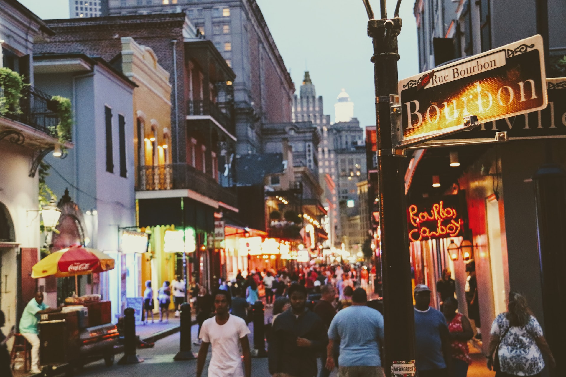 A street sign for Bourbon Street with people walking around.