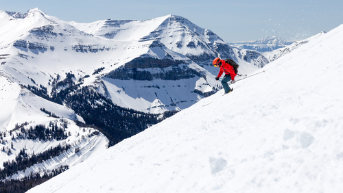 A solitary skier takes on the backcountry of Big Sky while wearing a ruby red parka with a matching red helmet.