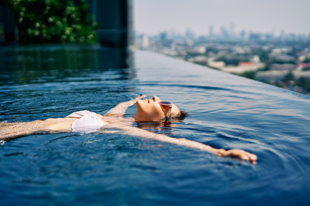 Young woman relaxing in roof top swimming pool and floating in water.