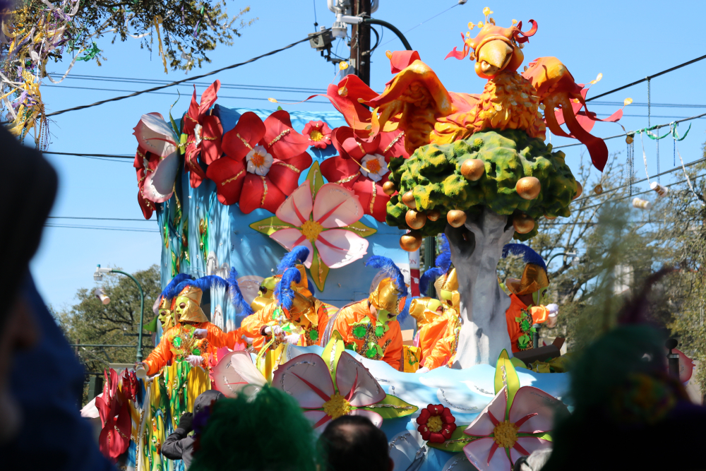 Mardi Gras float during midday with onlookers watching.
