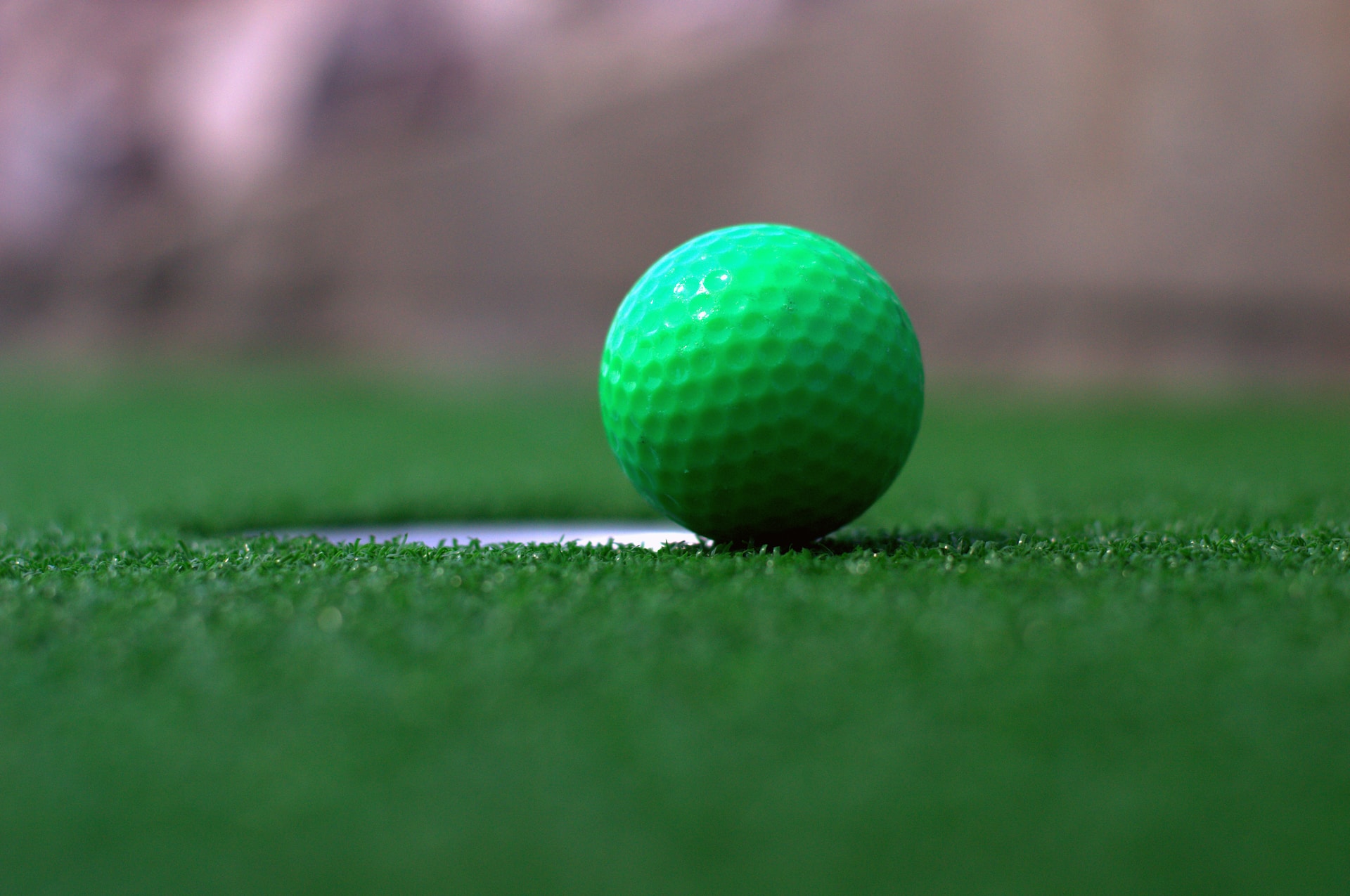Green golf ball on the edge of the hole.