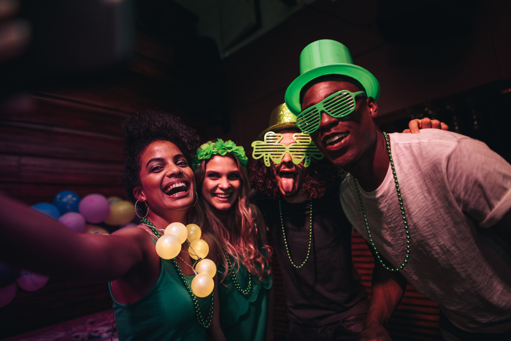 Group of friends enjoying at party in the bar and taking selfie with smart phone while wearing St. Patrick's Day attire.