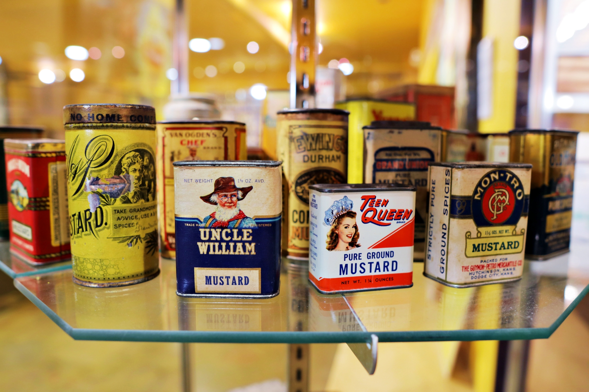 Different old school mustard tins on a glass exhibit.