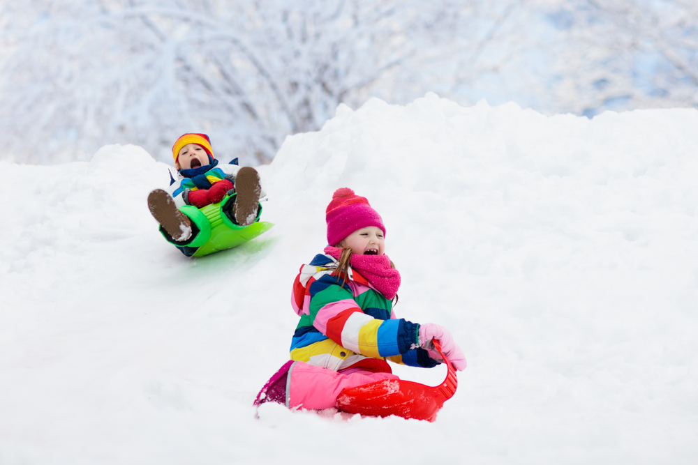 Children play outdoors in snow; kids sledding in snowy park in winter.