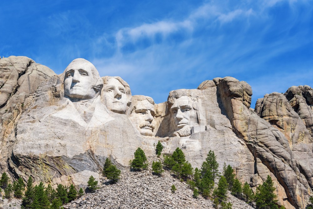 View of the four busts of George Washington, Thomas Jefferson, Theodore Roosevelt, and Abraham Lincoln on Mount Rushmore with a sunny day with blue sky.