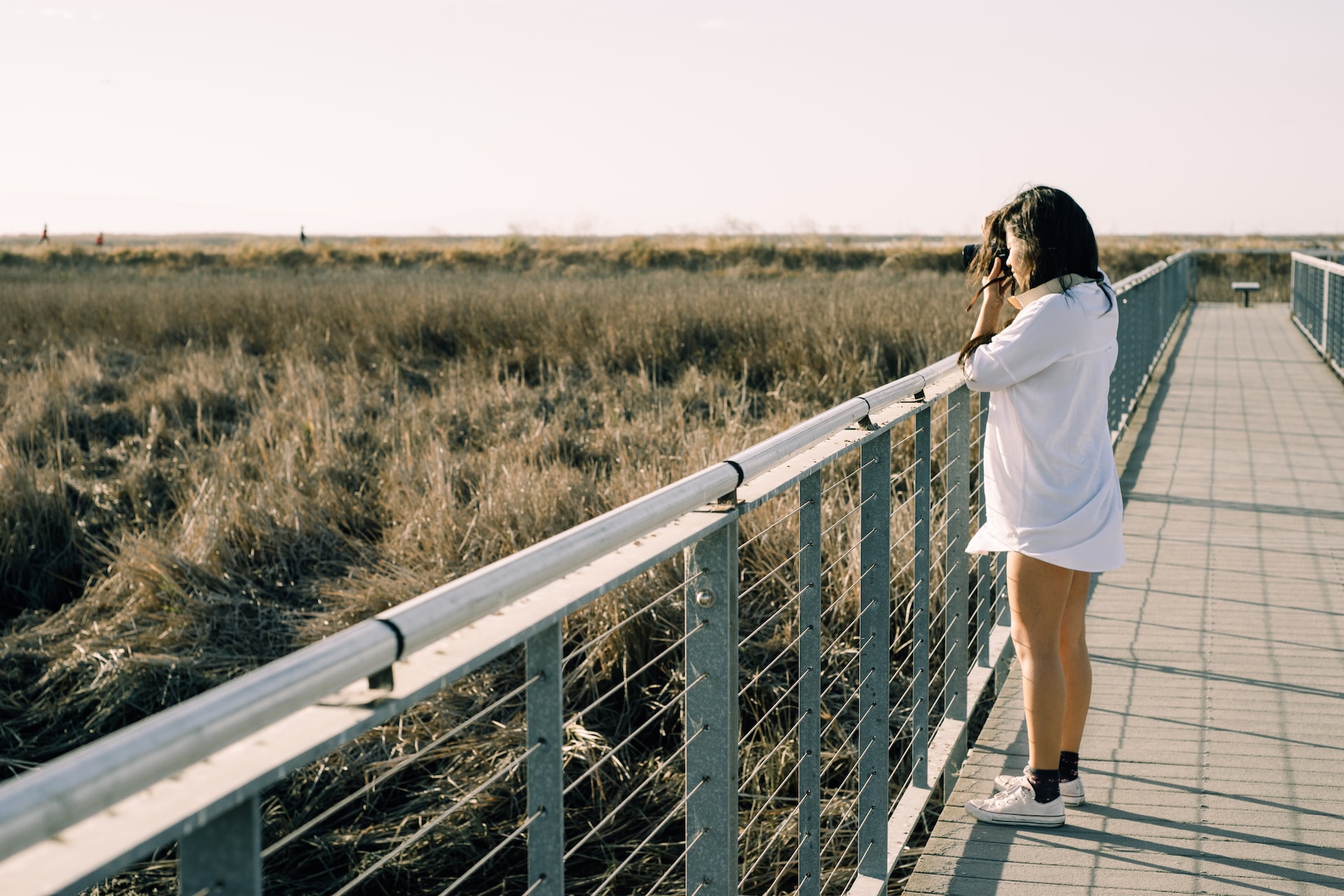 A woman taking pictures of the marsh from a boardwalk.