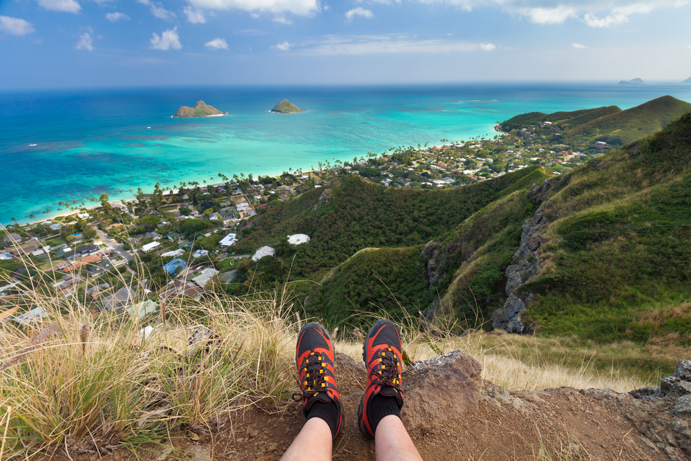 Two feet with boots in the foreground; a person enjoying the view of the Lanikai Pillboxes Trail in Oahu, Hawaii.