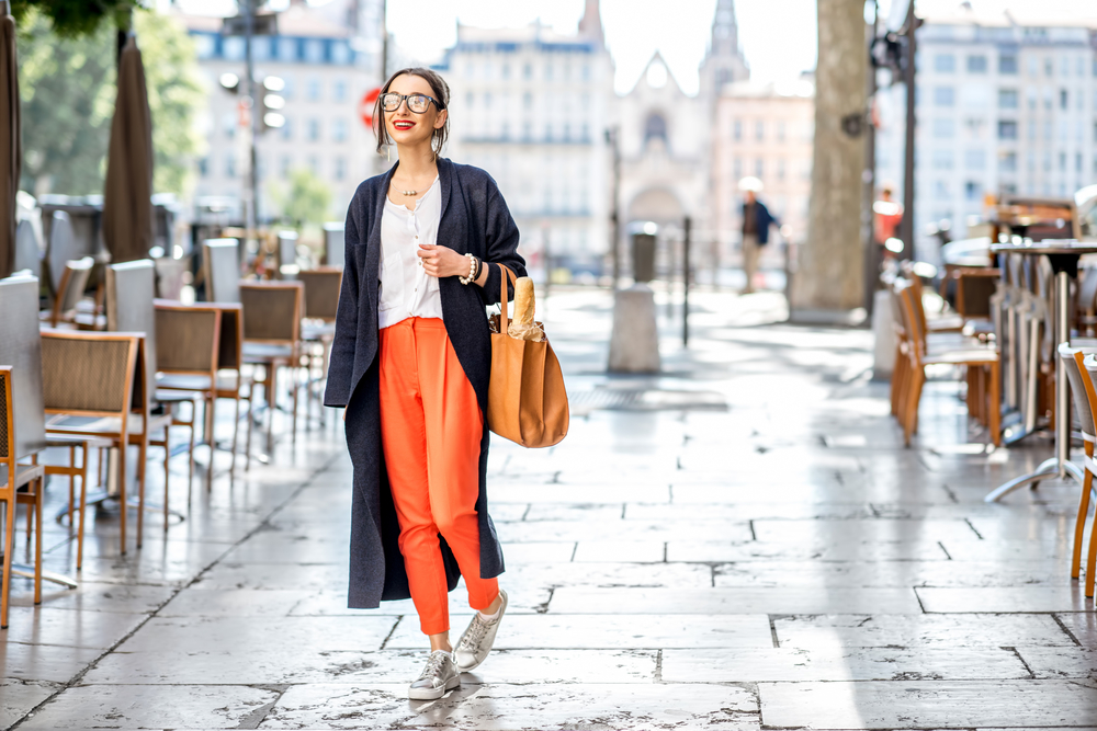 Lifestyle portrait of a French woman walking with a bag and baguette on a street lined with cafes in Lyon.
