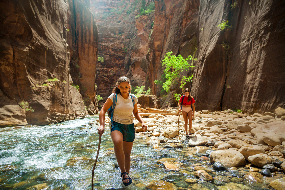 Two female hikers trekking the Narrows in Zion National Park.