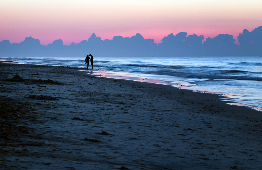 Couple walking on sunrise beach.