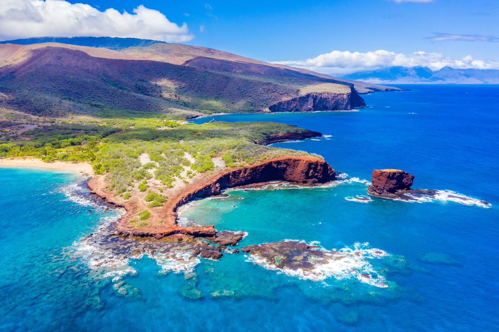 Aerial view of Lanai, Hawaii, featuring Hulopo'e Bay and beach, Sweetheart Rock (Pu'u Pehe), Shark's Bay, and the mountains of Maui in the background.