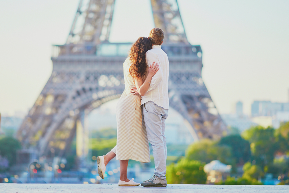 A couple with their backs turned stare at the Eiffel Tower in the distance.