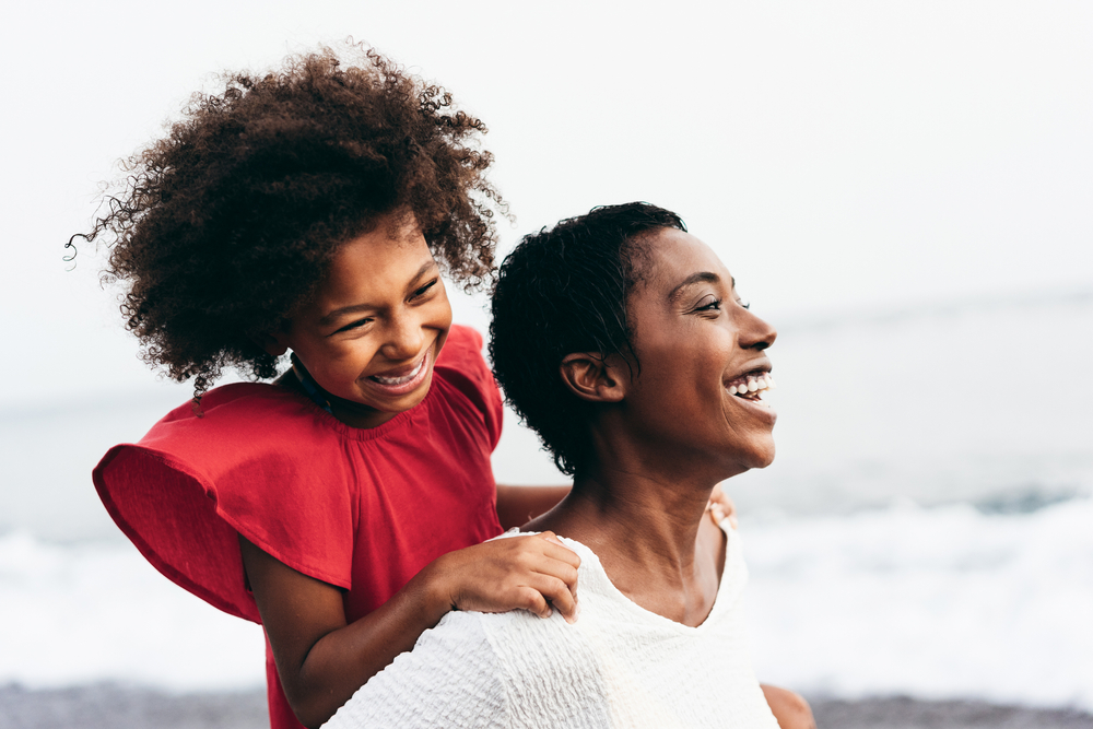 Mother and daughter on her back smiling at the beach.