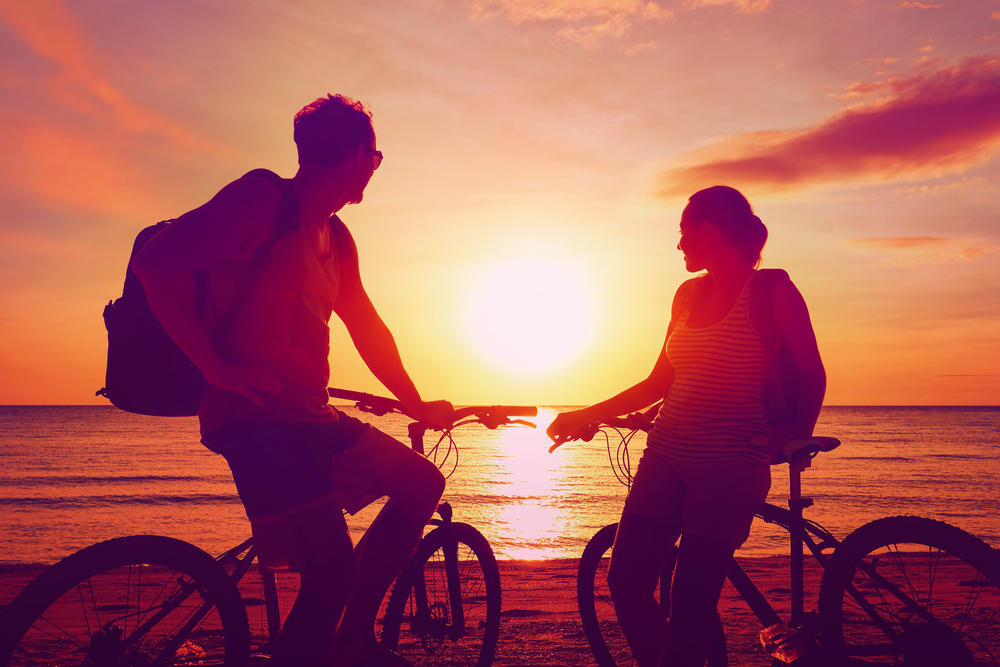 Couple tourists with bicycles watching the sunset on the beach.