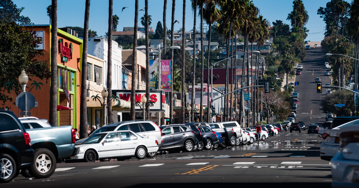 The tree-lined road and storefronts of Newport Avenue.