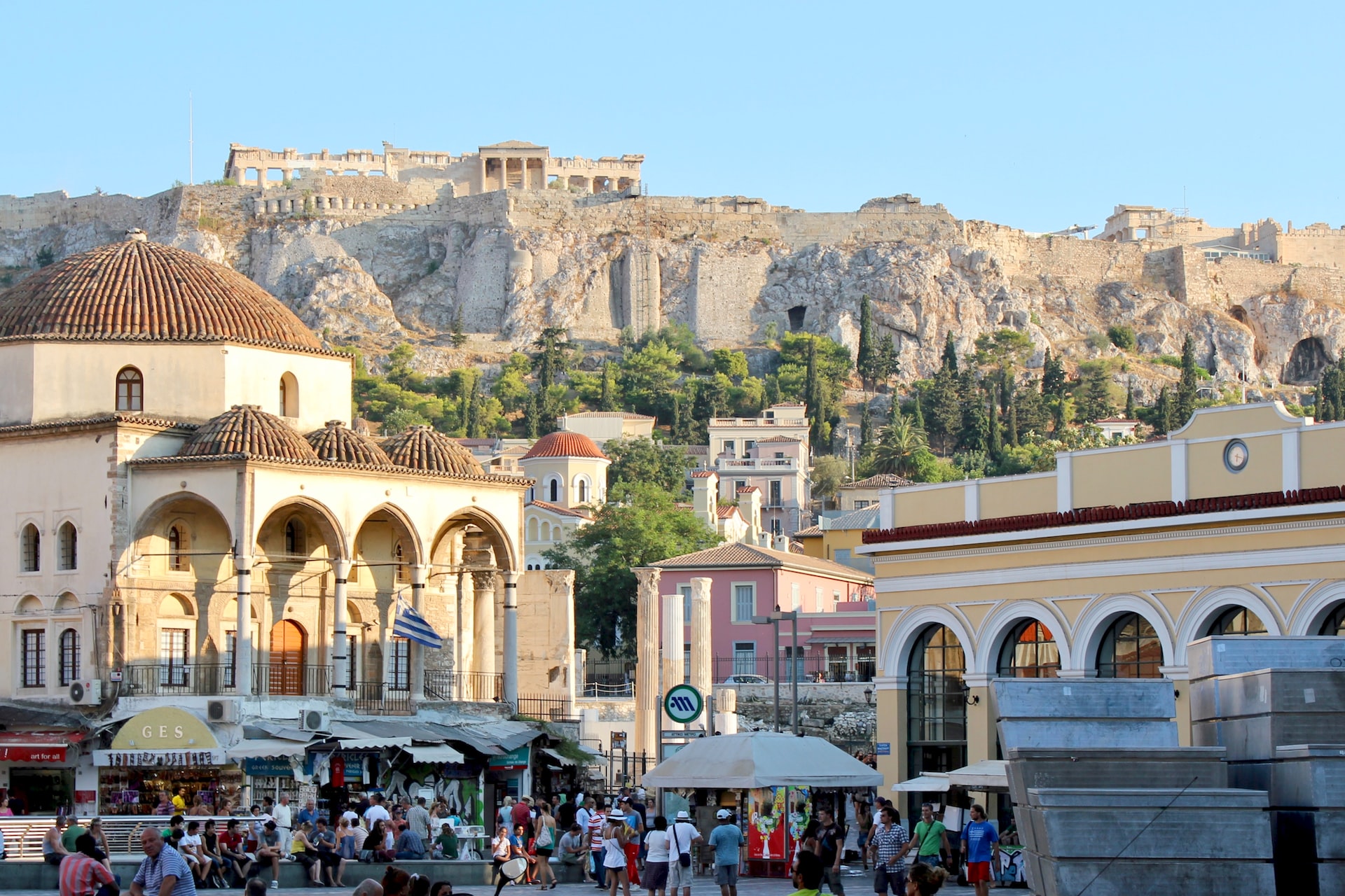 People walking along the busy streets in Athens with the Acropolis in the distance.