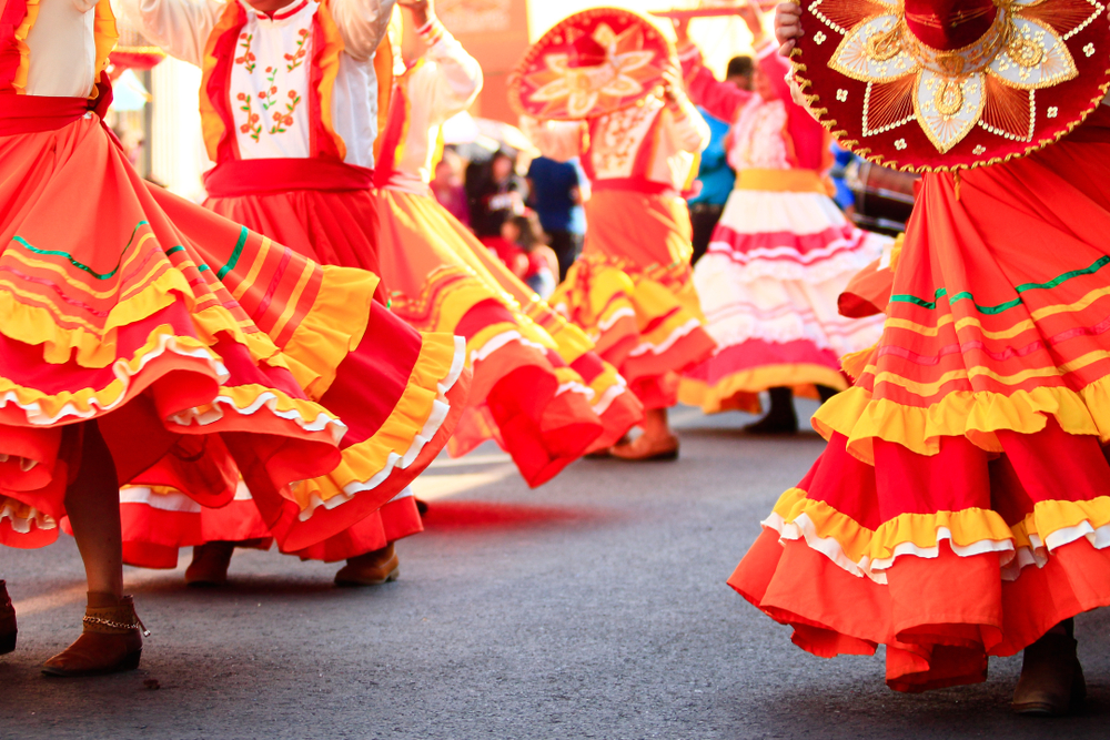 Women wearing traditional Spanish dresses parading down the street.