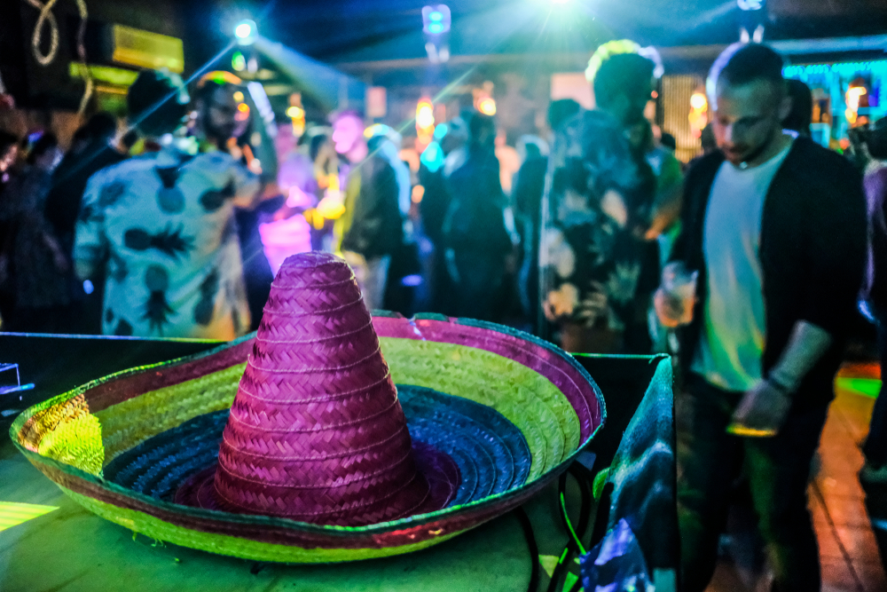 Colorful sombrero in the foreground with people dancing at a bar.
