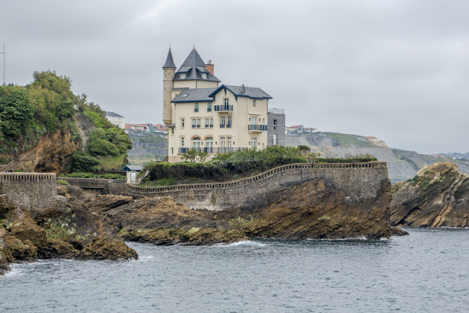 A newer looking castle surrounded by an older looking stone wall on a small peninsula connected to the mainland.