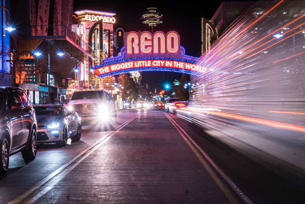 A car speeding in a blur underneath the bright lights of the Reno sign.