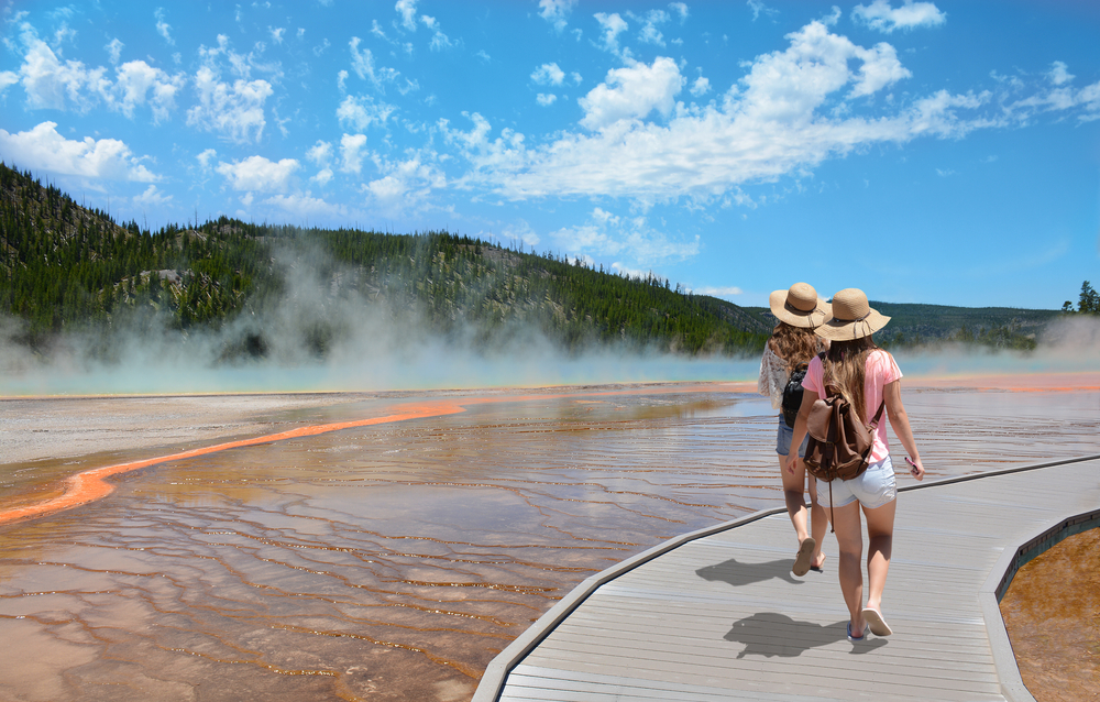 Girls wearing hats hiking on vacation at the beautiful Grand Prismatic Spring in Yellowstone National Park.