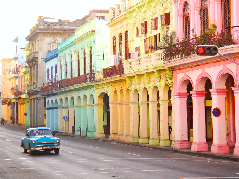 An old vintage car driving past the colorful buildings in Havana.