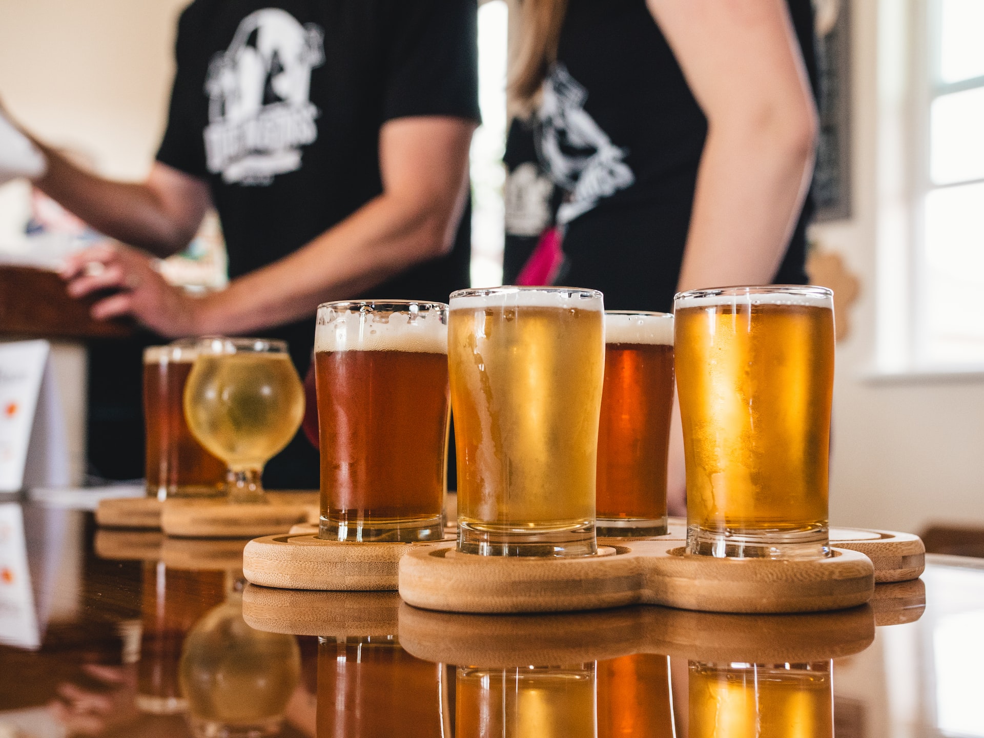 Two bartenders in matching shirts standing behind a tray of different sized beers on a bar counter.