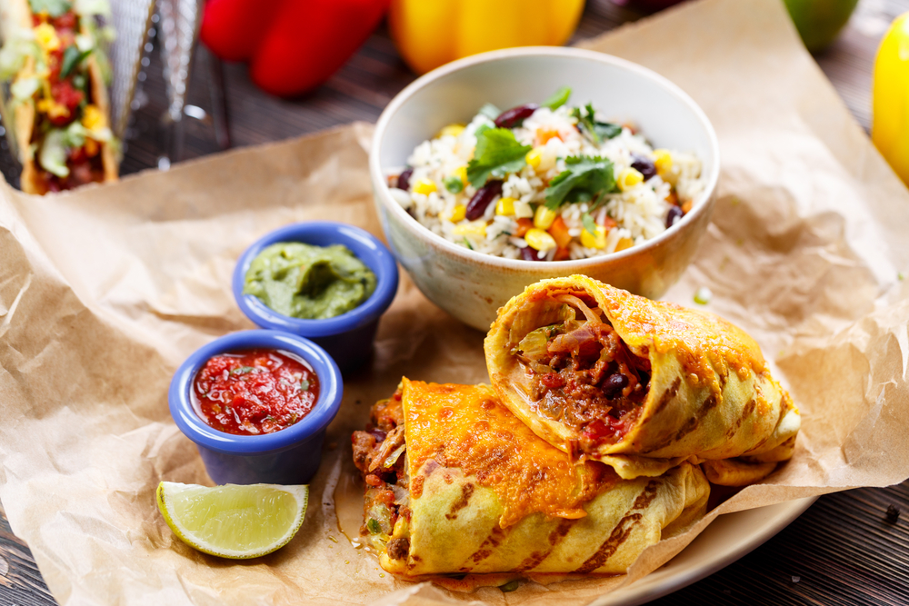 A delicious-looking burrito with two sauces and a lime with a side.