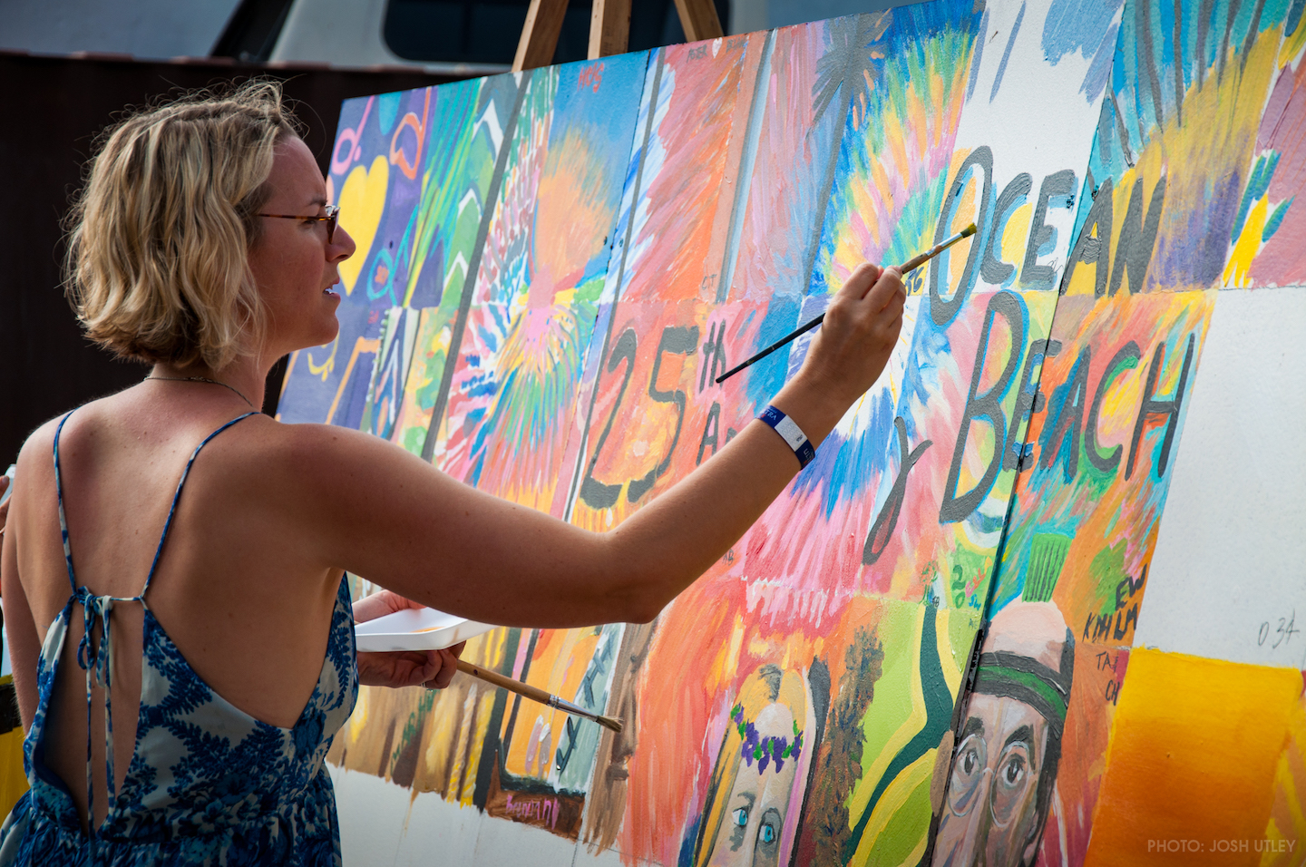 Woman painting a mural outside in a sundress.